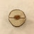 A wooden slice with concentric rings is placed on a light fabric background. At the center, a small heart-shaped piece with the word 'Love' engraved on it is embedded in the wood.