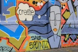 Colorful graffiti art on a wall featuring geometric shapes, a speech bubble with the word 'create', and a stylized face with closed eyes and orange lips. Text 'SAVE 5 POINTZ' is also visible.