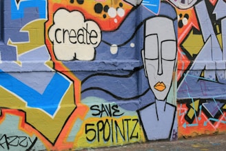 Colorful graffiti art on a wall featuring geometric shapes, a speech bubble with the word 'create', and a stylized face with closed eyes and orange lips. Text 'SAVE 5 POINTZ' is also visible.