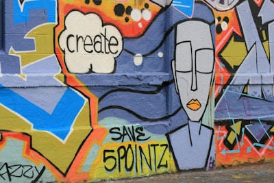 Colorful graffiti art on a wall featuring geometric shapes, a speech bubble with the word 'create', and a stylized face with closed eyes and orange lips. Text 'SAVE 5 POINTZ' is also visible.
