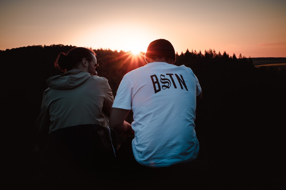 Mann im weißen Rundhals-T-Shirt steht bei Sonnenuntergang neben einer Frau in schwarzer Jacke