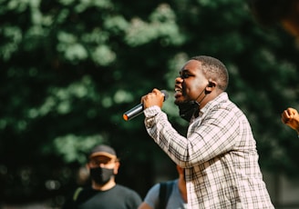 man in blue and white plaid dress shirt holding microphone