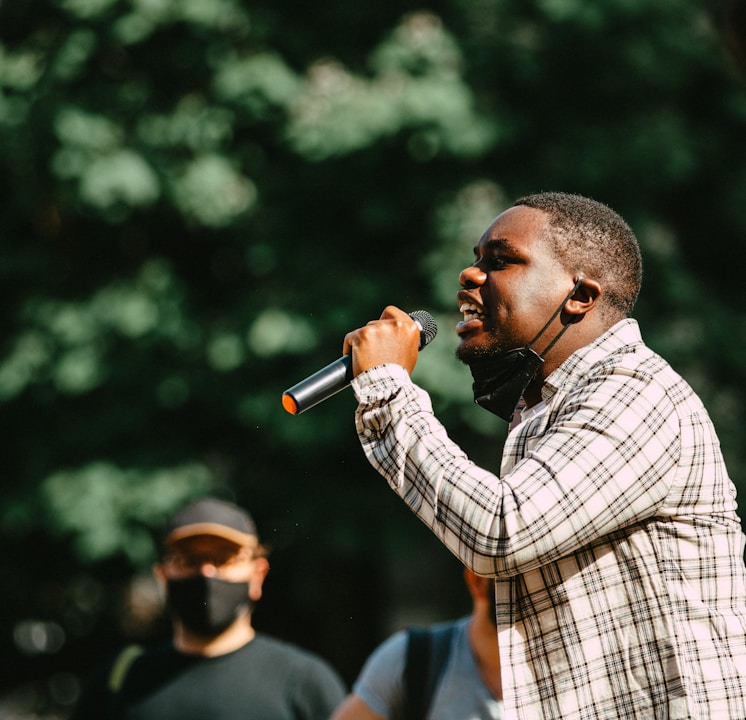 man in blue and white plaid dress shirt holding microphone