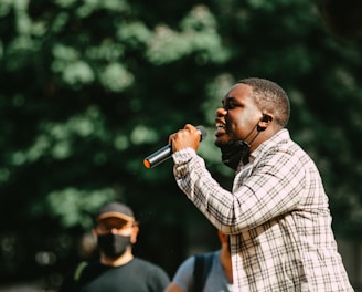 man in blue and white plaid dress shirt holding microphone