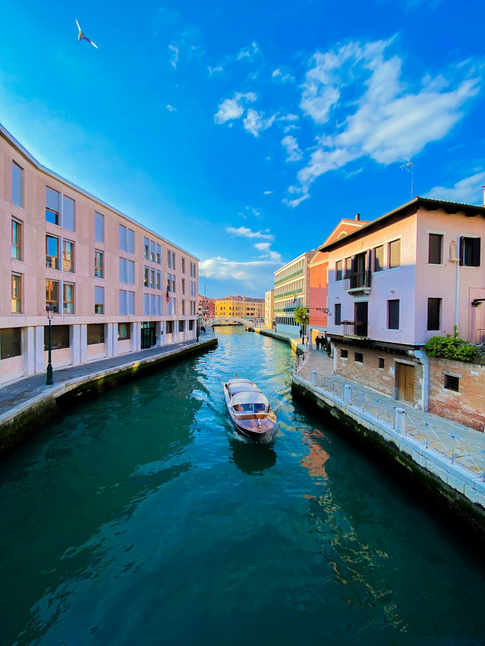 boat on river between buildings under blue sky during daytime