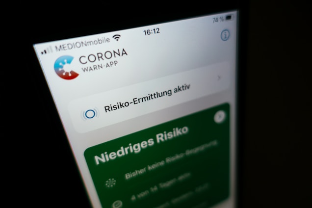A close-up of a smartphone screen displaying the Corona Warn-App, with active risk assessment shown in German. The status indicates 'low risk' with additional text providing more information.