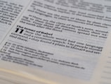 The image displays an open page of a Bible with a focus on a passage from Genesis 11, discussing the Tower of Babel. The text is clearly printed, highlighting themes of language and communication.