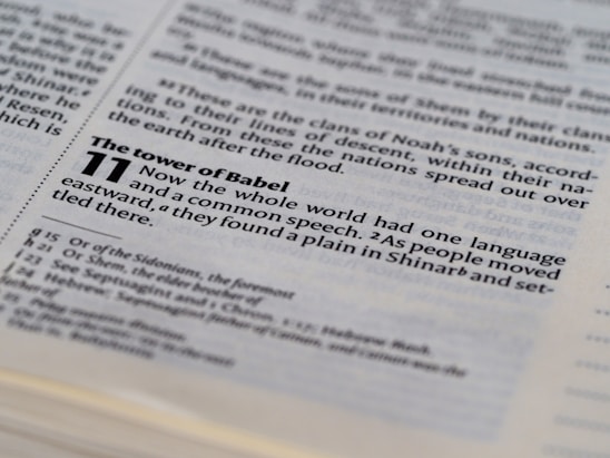 The image displays an open page of a Bible with a focus on a passage from Genesis 11, discussing the Tower of Babel. The text is clearly printed, highlighting themes of language and communication.