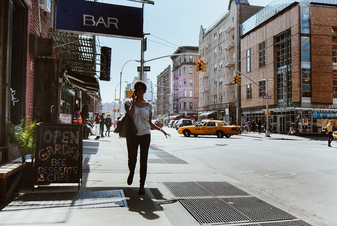 woman in gray coat and white pants walking on pedestrian lane during daytime