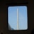A bridge with a tall, sleek metallic tower is seen through a window, with multiple cables extending from the tower against a clear blue sky.
