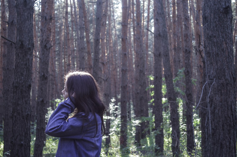 woman in blue jacket standing in the woods