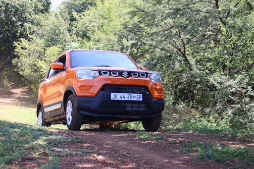 Close-up of a sleek orange SUV driving on a sandy path with tropical greenery.
