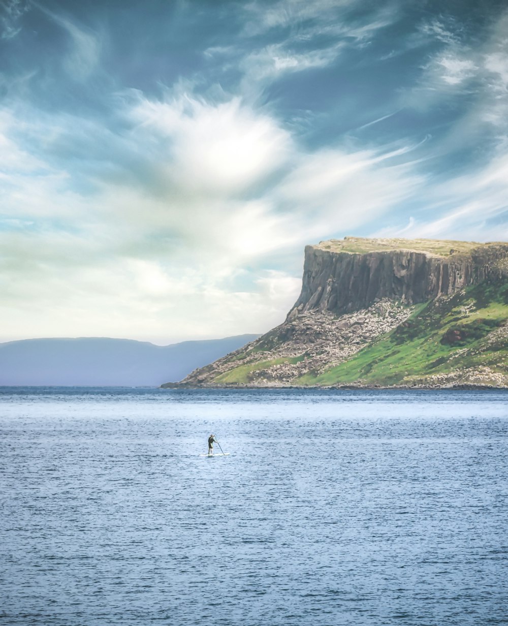 people riding boat on sea near brown mountain under blue sky during daytime