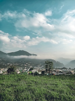 green grass field near mountain under white clouds during daytime