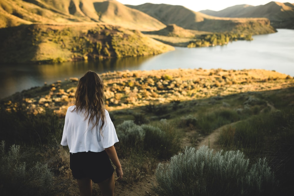 woman in white shirt standing on green grass near lake during daytime