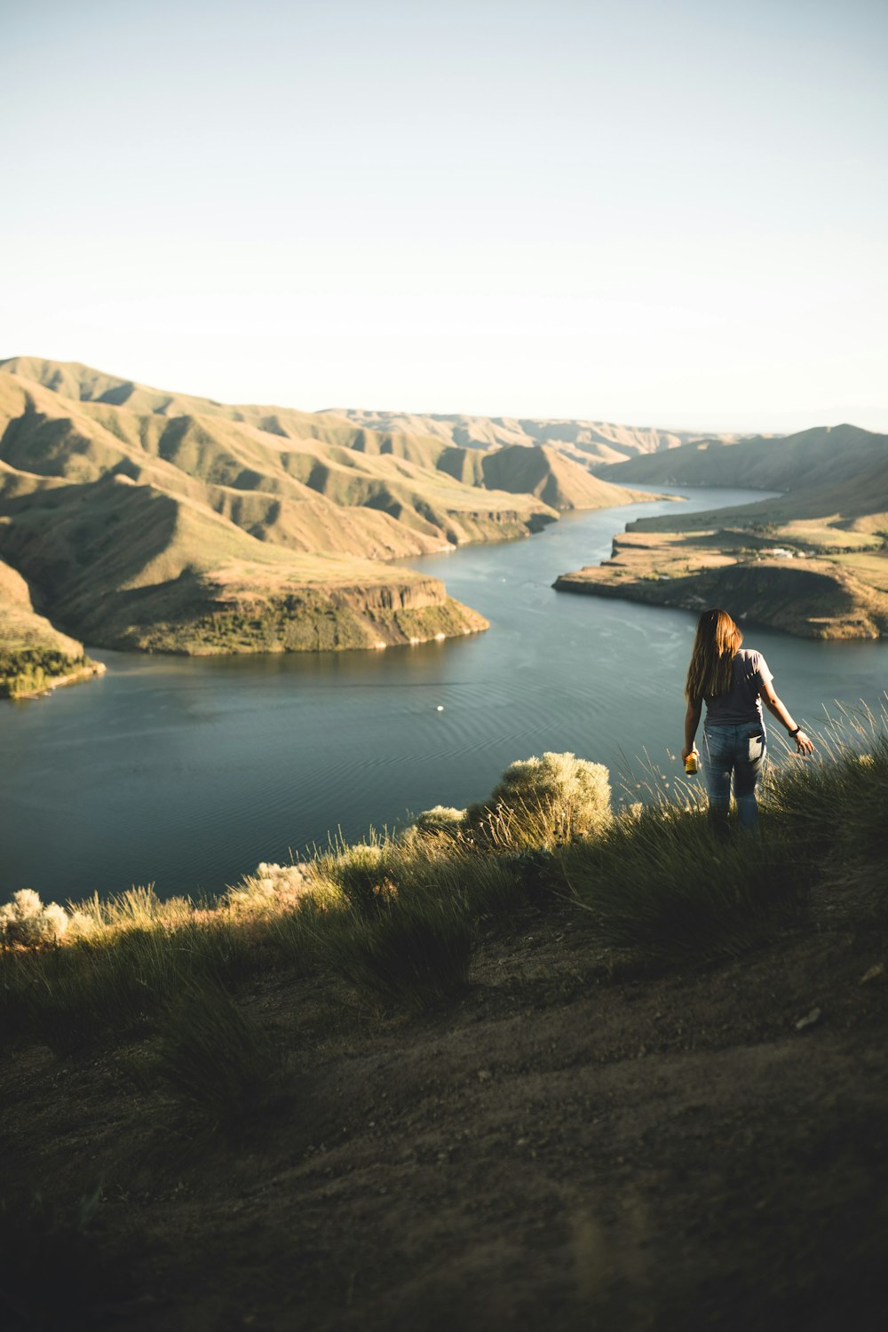 woman in black jacket standing on green grass near lake during daytime