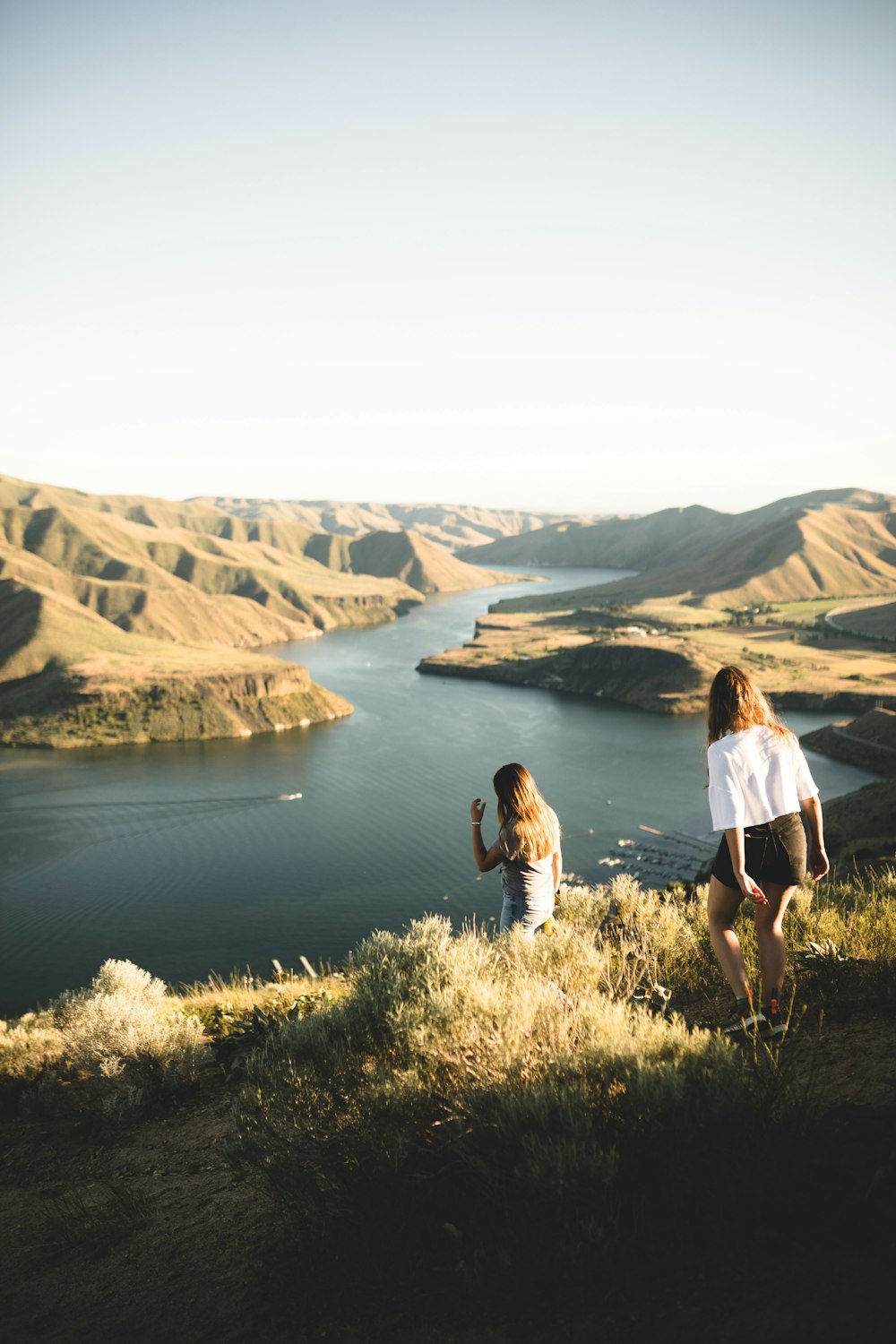 woman in white shirt standing on green grass field near lake during daytime