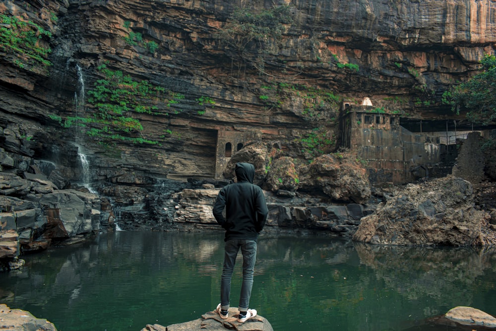 man in black jacket standing on rock formation near body of water during daytime