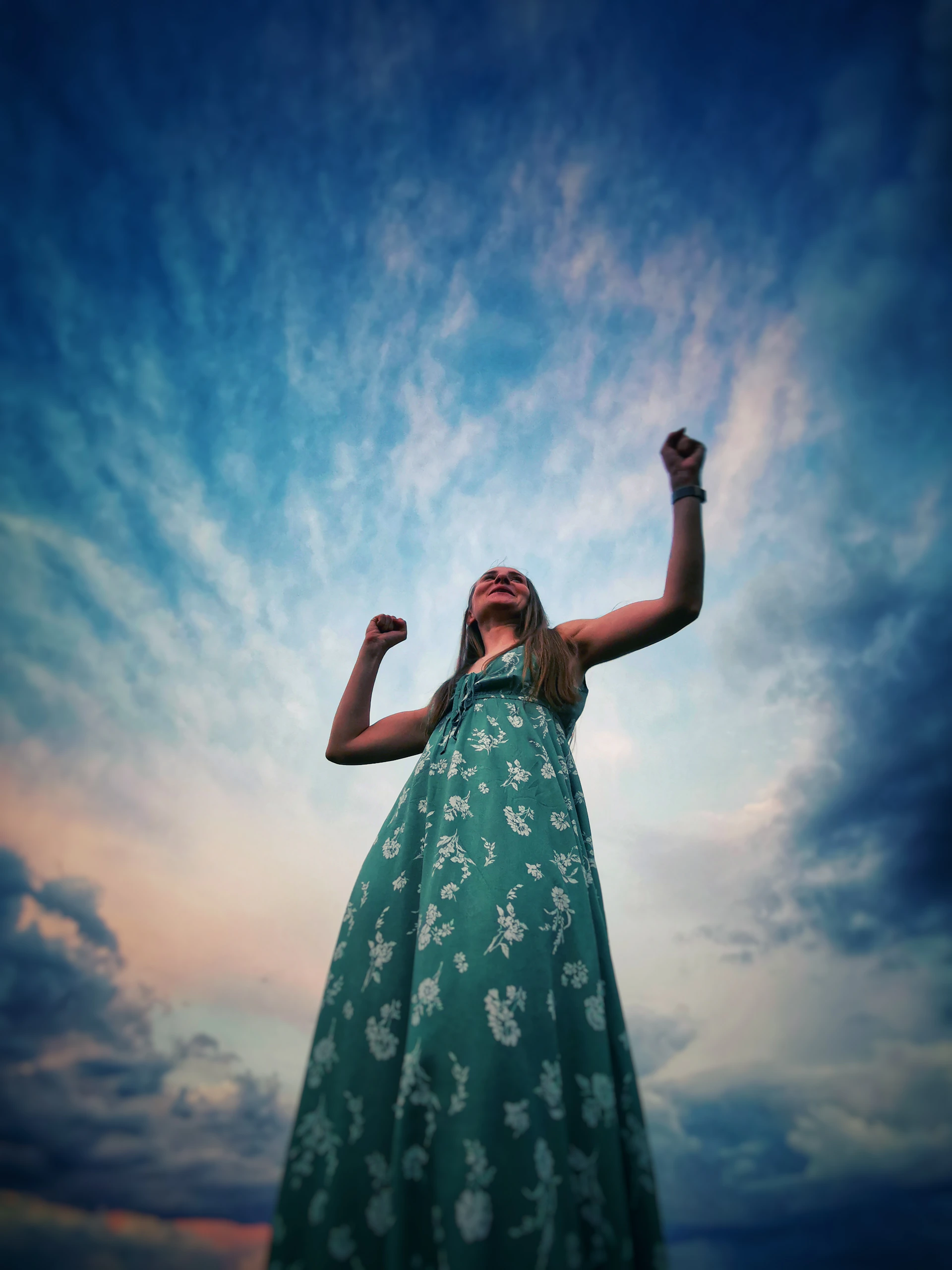 woman in blue and white floral dress raising her right hand under blue sky during daytime