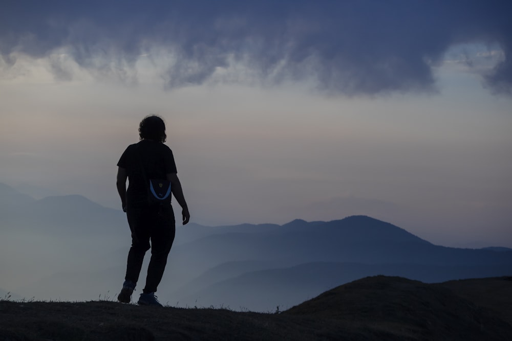 homem em jaqueta preta em pé no topo da montanha durante o dia