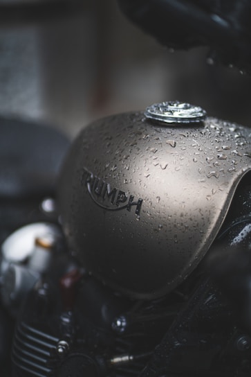 A close-up view of a motorcycle fuel tank covered in water droplets, with the brand name prominently displayed on the tank.