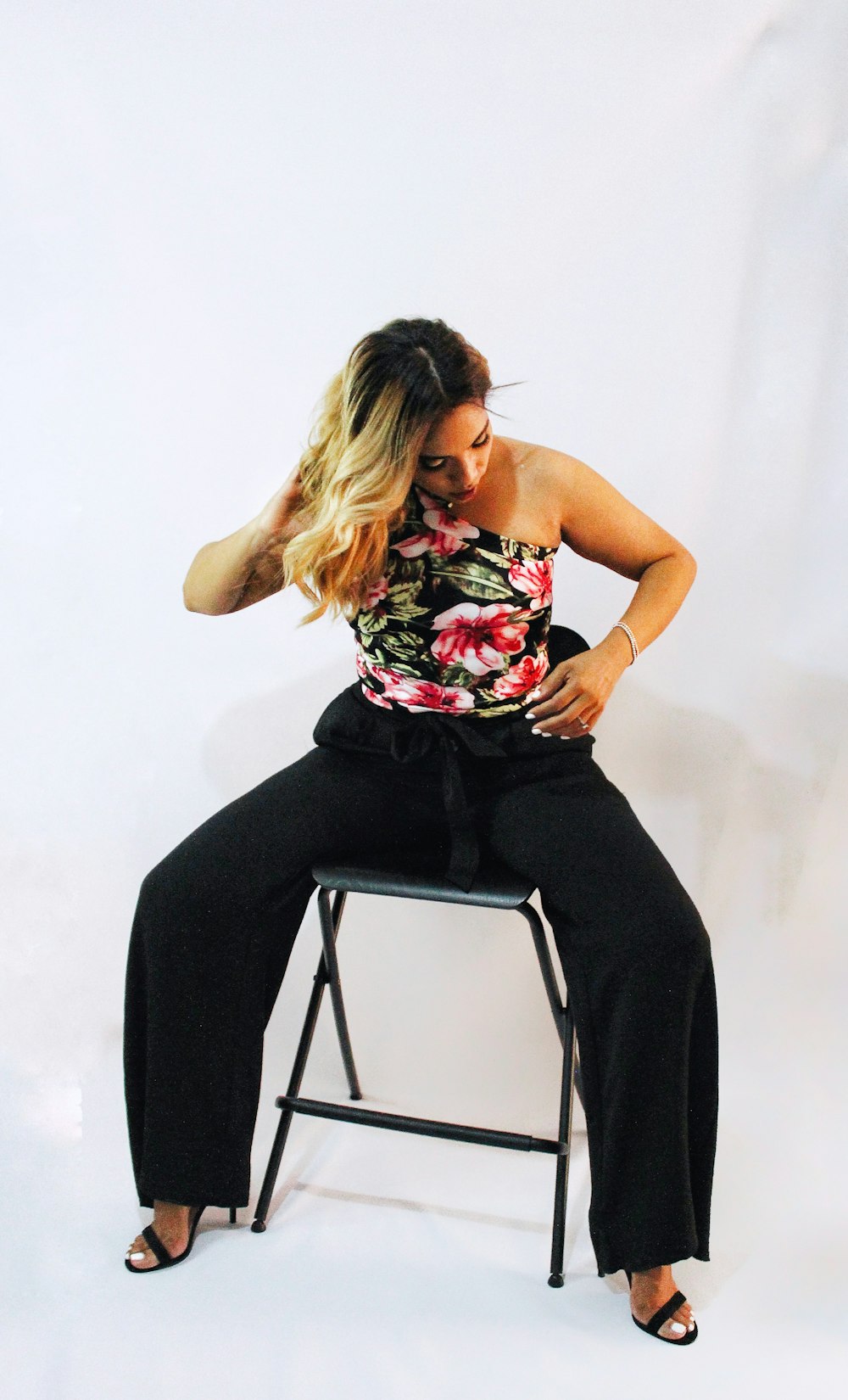 Woman in black and red floral tank top and black pants sitting on