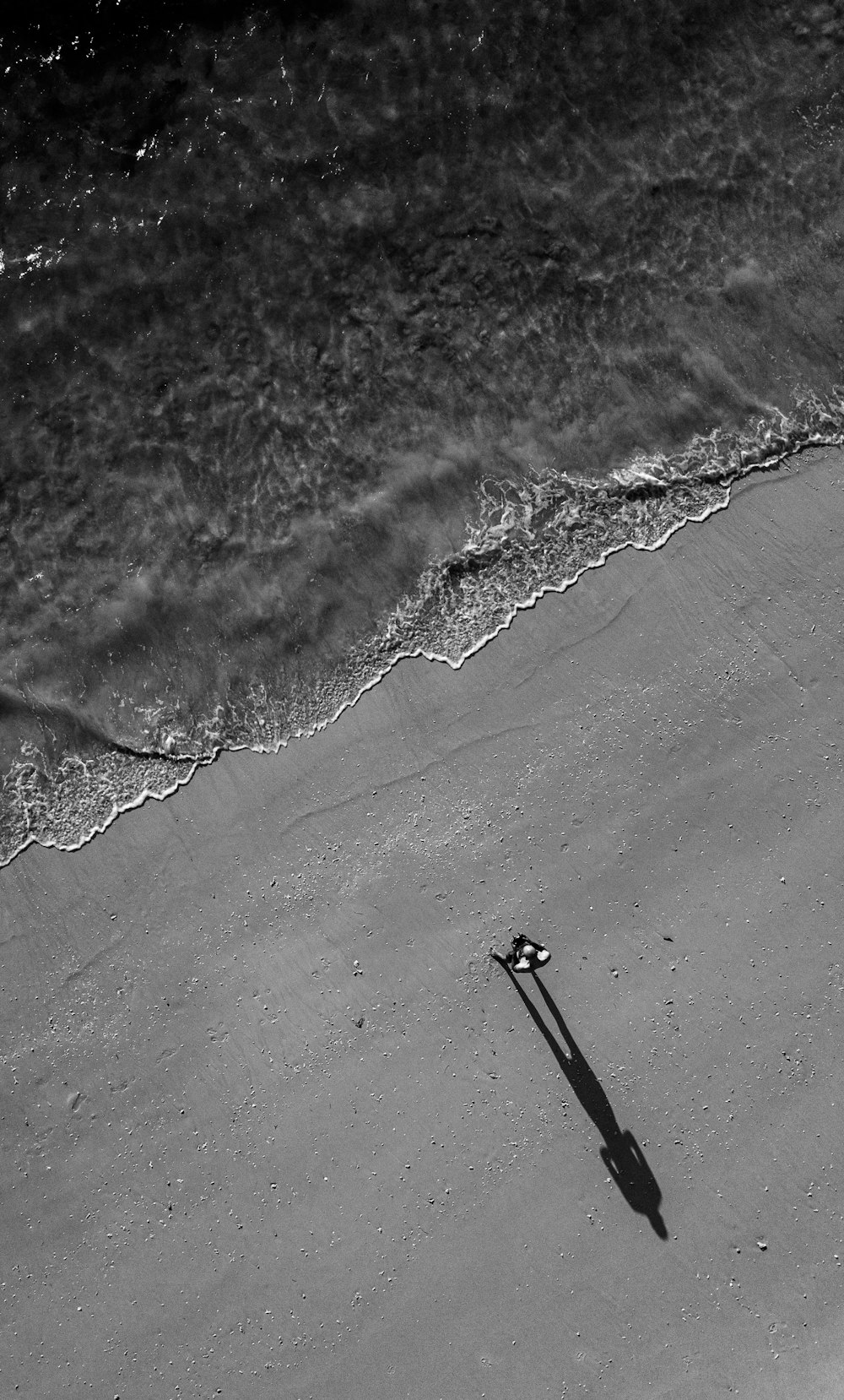 Graustufenfoto einer Person, die am Strand spazieren geht