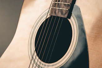 Close-up of a vintage acoustic guitar with warm brown and orange hues against a deep black background, subtle parallax effect.