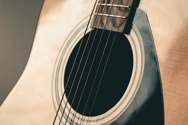 Close-up view of an acoustic guitar focusing on the strings and soundhole, with the wooden texture and subtle lighting creating a warm and inviting feel.
