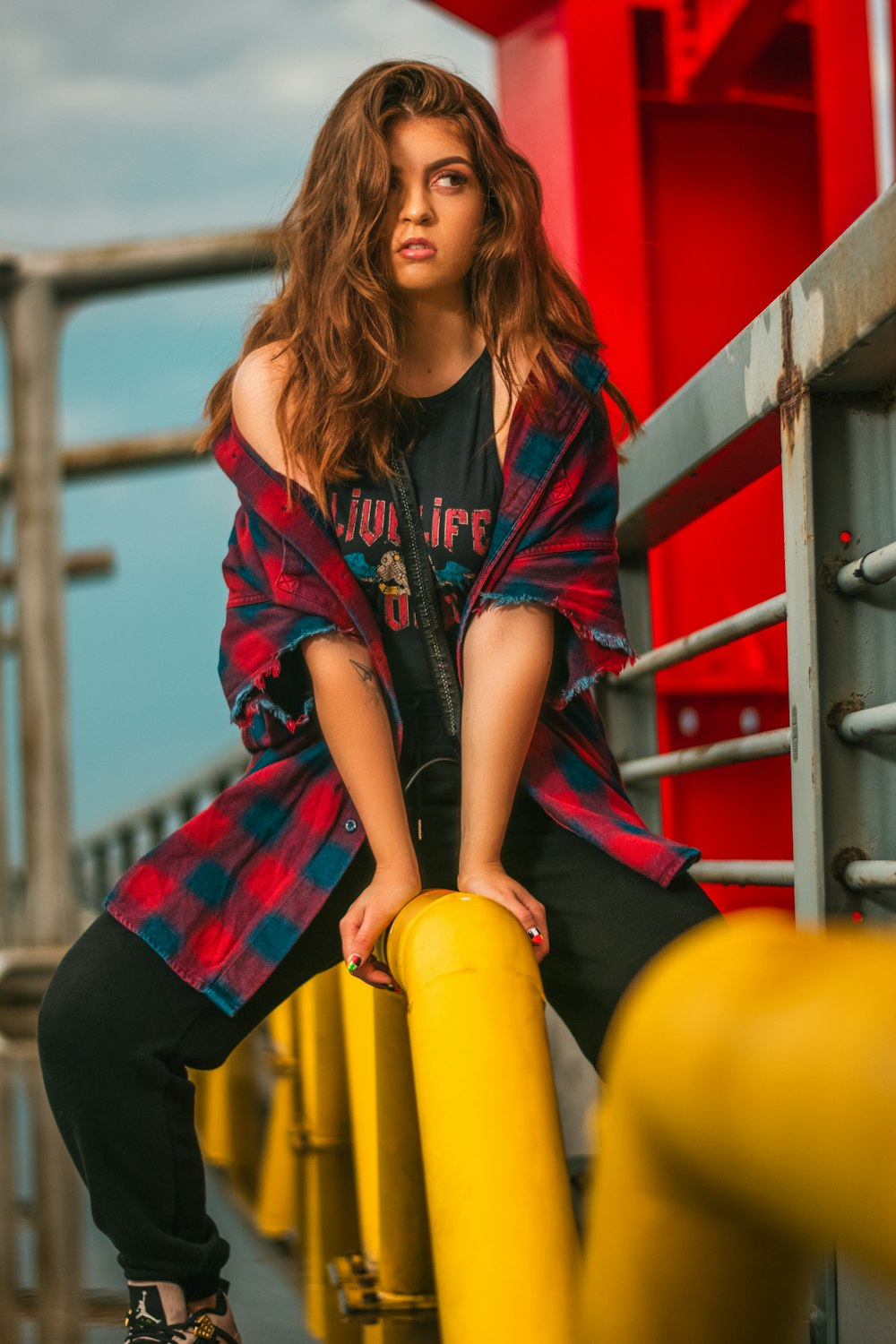 woman in red and black zip up jacket and black pants sitting on yellow metal pipe