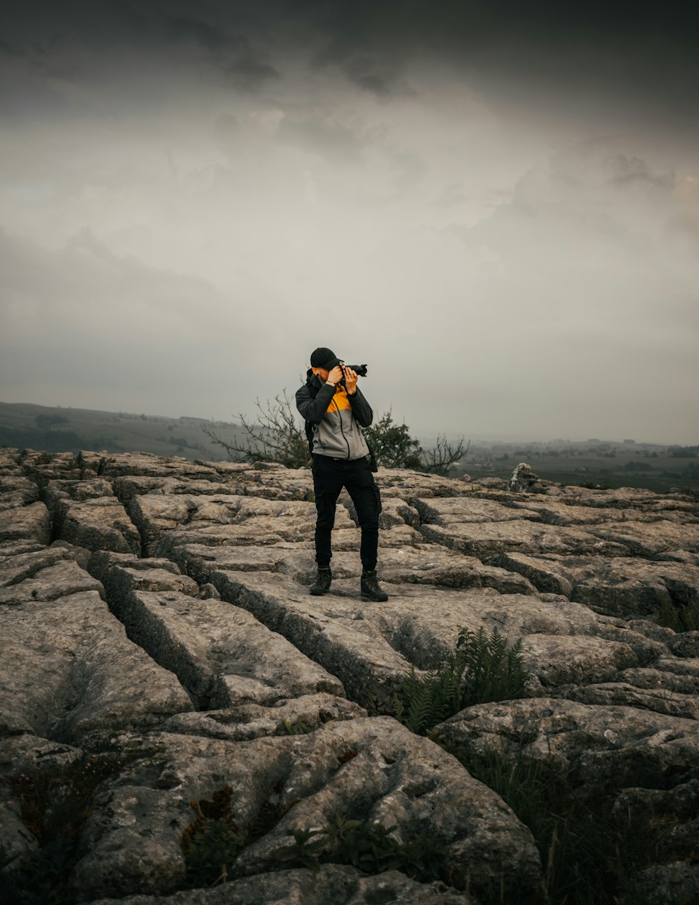 man in black jacket and black pants standing on brown rock formation under gray cloudy sky