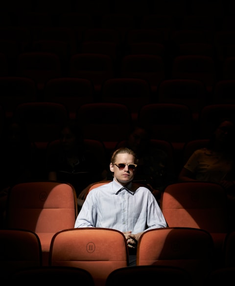 man in blue dress shirt wearing sunglasses sitting on brown chair