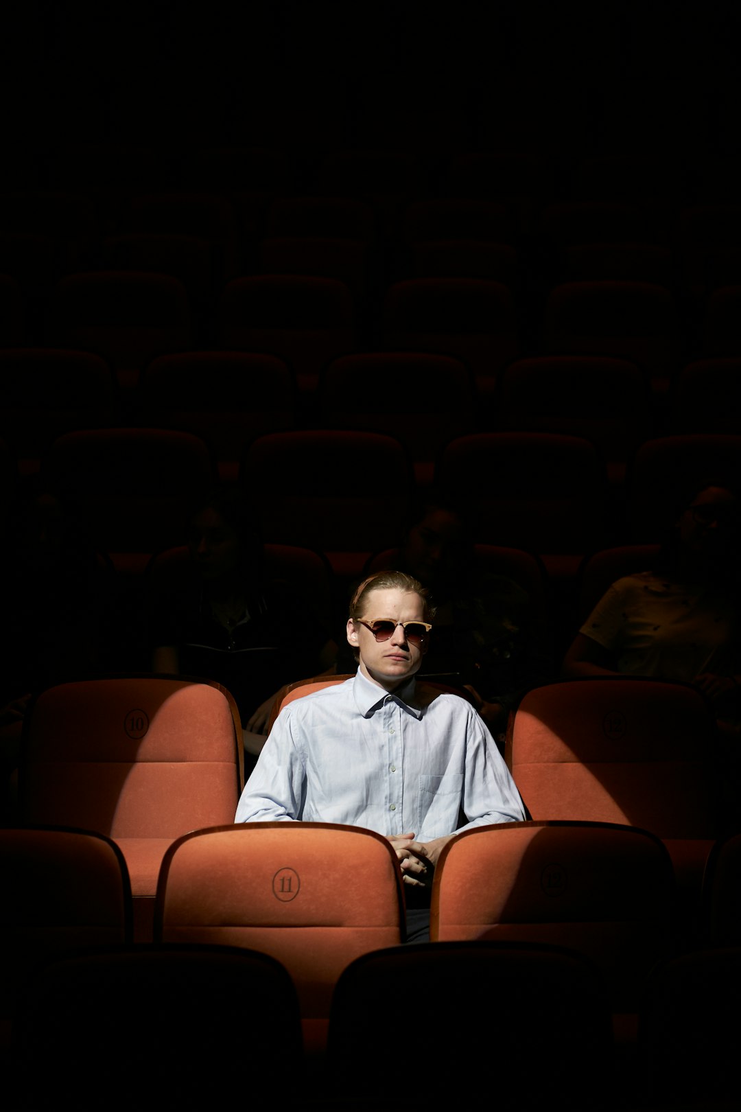 A lone man sitting under the spotlight in the theatre hall.