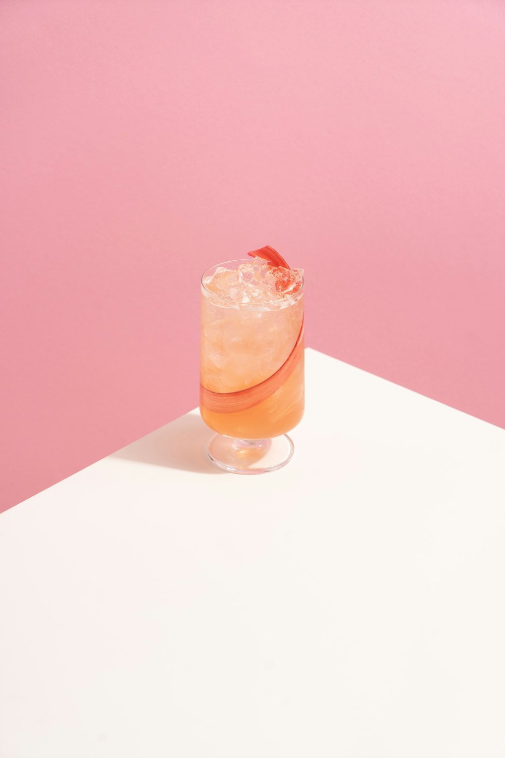 verre à boire transparent avec un liquide orange sur une table blanche