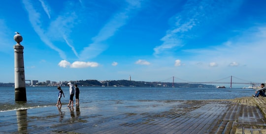 man and woman walking on beach during daytime in Praça do Comércio Portugal