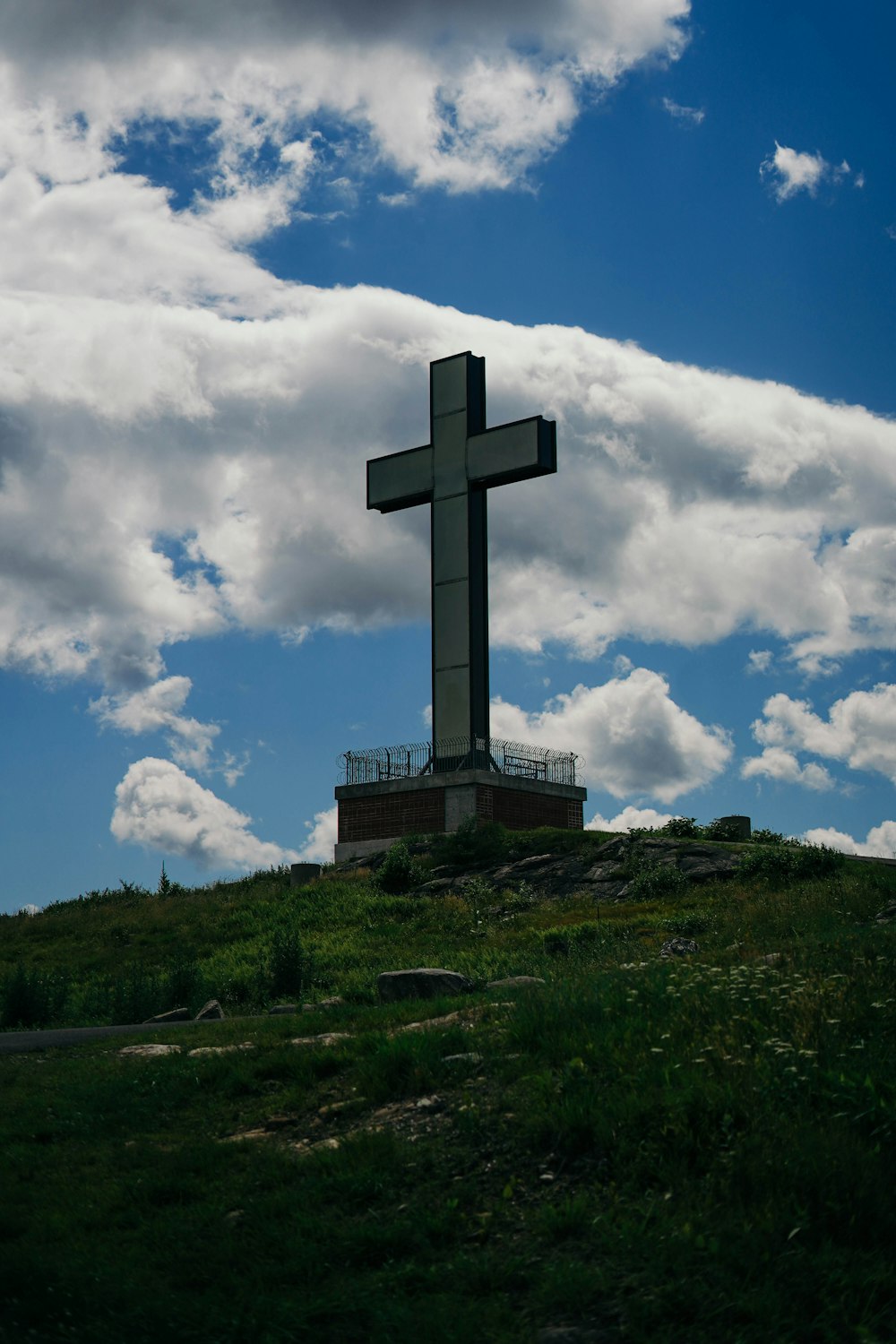 gray cross on green grass under white clouds and blue sky during daytime