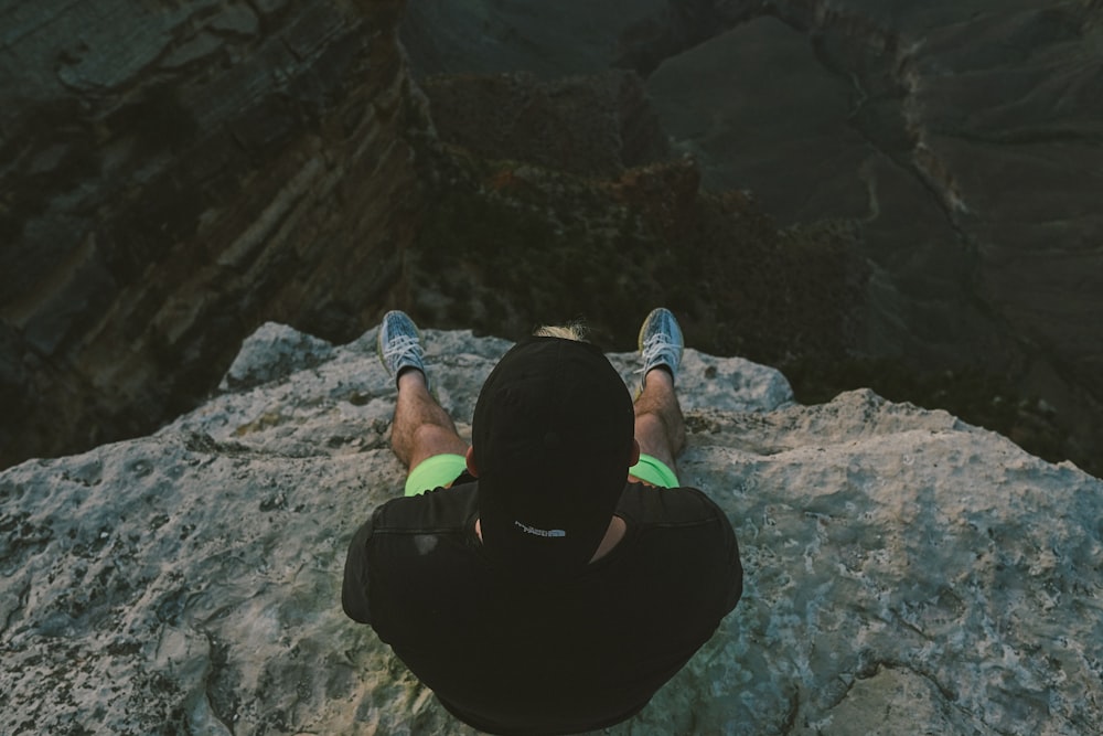 person in black hoodie sitting on rock formation during daytime