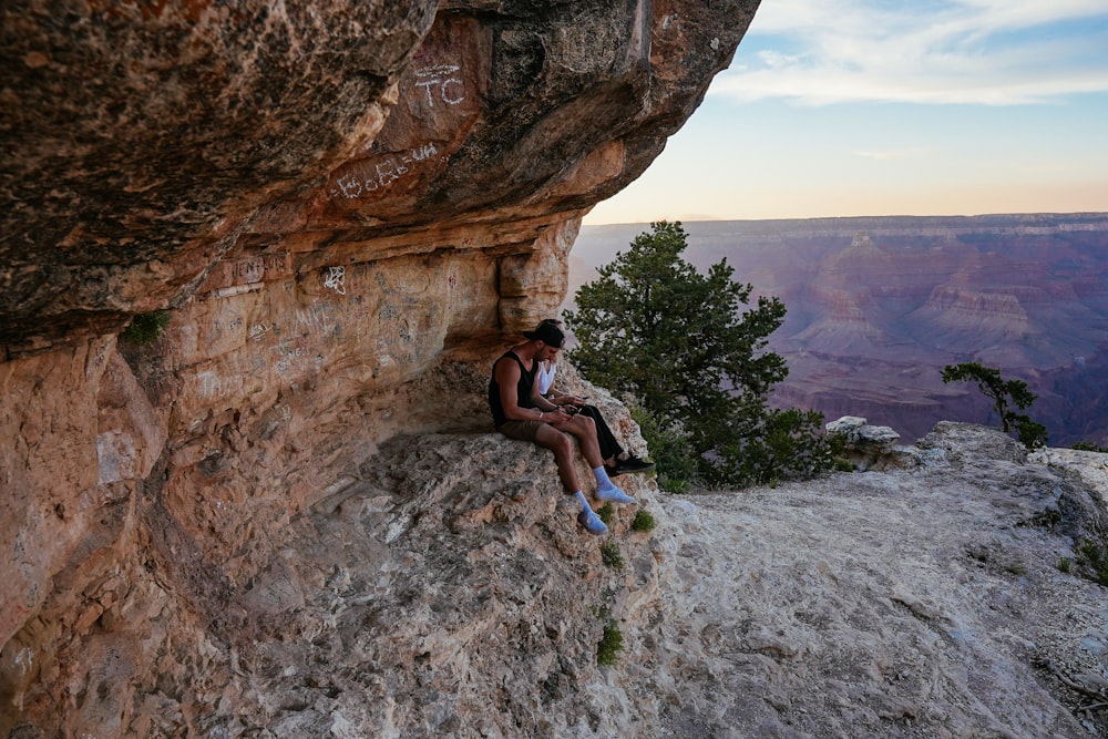 woman in black tank top and white pants sitting on brown rock formation during daytime
