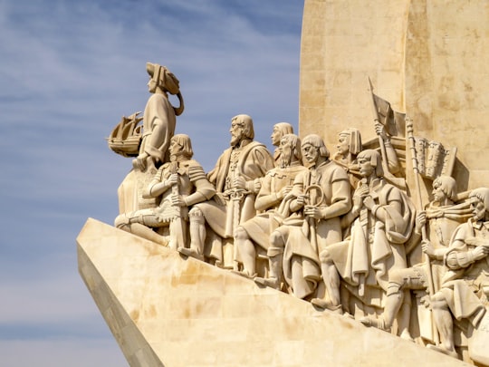 people sitting on concrete statue under blue sky during daytime in Padrão dos Descobrimentos Portugal