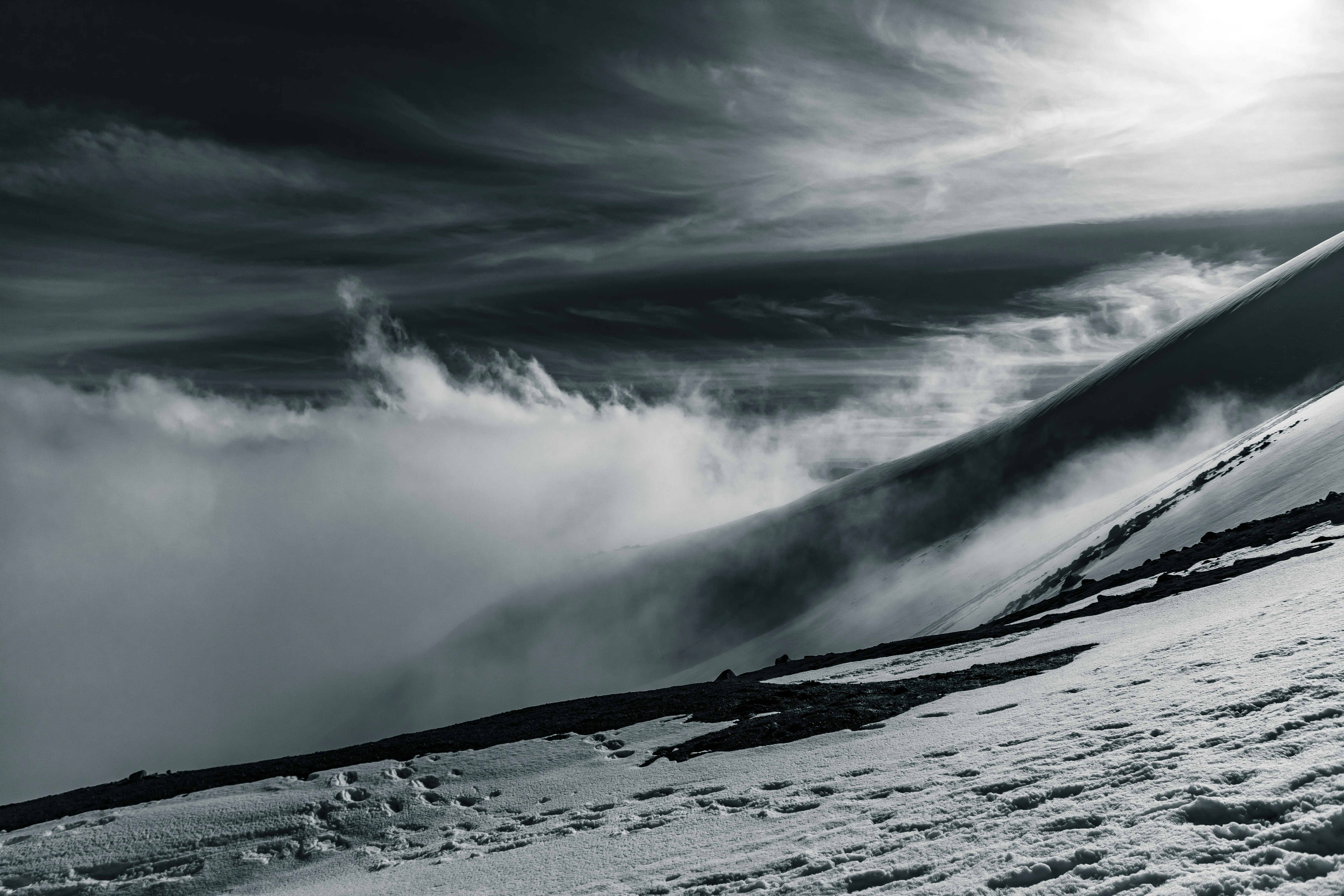 grayscale photo of snow covered mountain under cloudy sky
