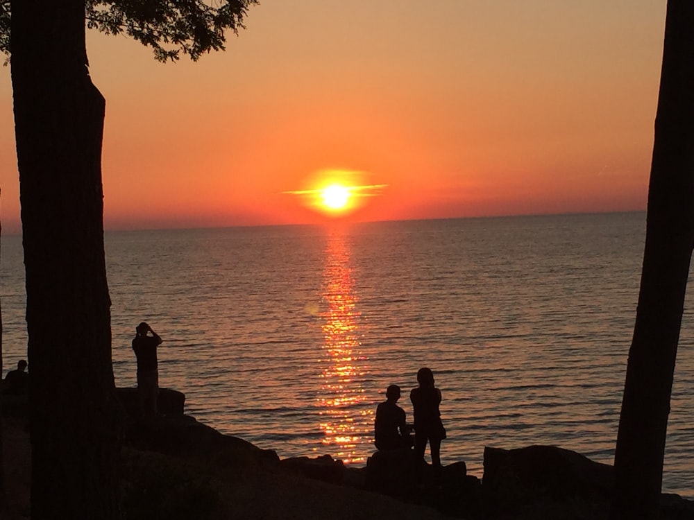 silhouette of 2 people sitting on rock near body of water during sunset