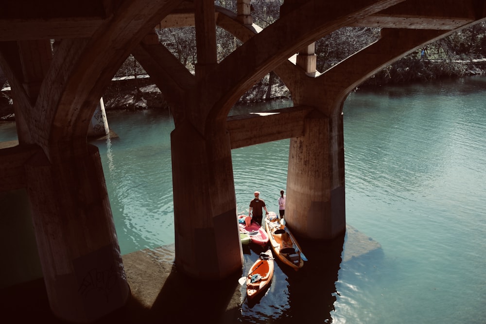 2 person riding on blue and red boat under brown concrete bridge during daytime