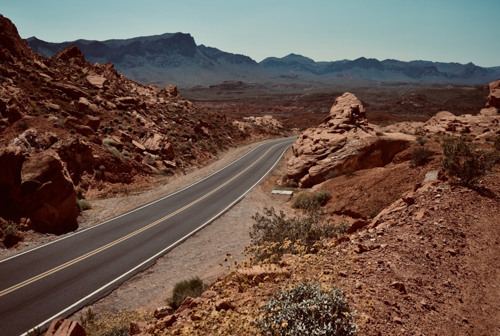 gray asphalt road between brown rock formation during daytime