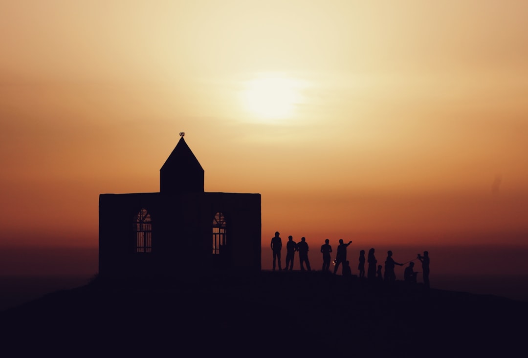 silhouette of people standing near church during sunset
