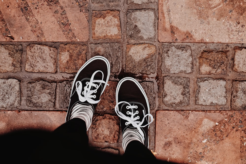 personne en baskets noires et blanches debout sur un sol en briques brunes