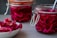 Two glass jars filled with vibrant red sauerkraut and a bowl of the same cabbage are placed on a gray surface. The jars feature metal latch lids, and a spoon is sticking out of the closer jar.