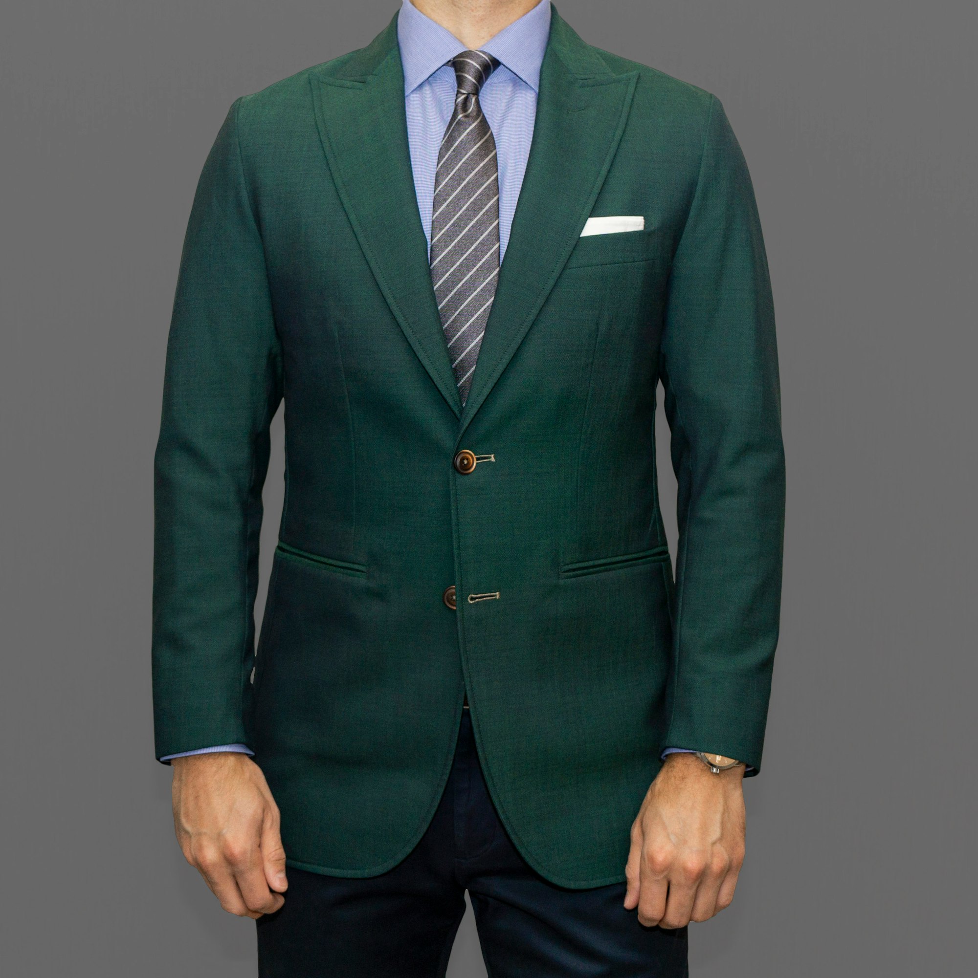 Dapper Professional wearing a green blazer, blue shirt and gray striped tie. The blazer is a customer blazer with wide peak labels, pick stitching and contrast, functional button holes. 