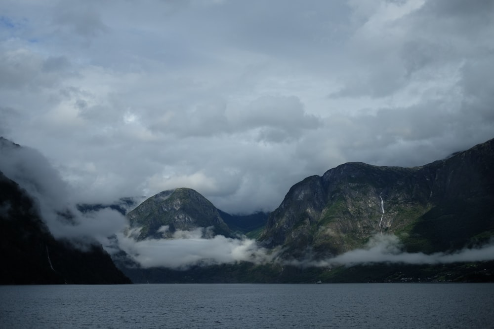 body of water near mountain under cloudy sky during daytime