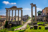 Historic Roman ruins bathed in warm afternoon light with tourists exploring.