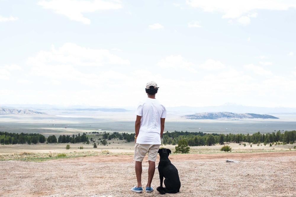 man in white t-shirt and black shorts holding black short coated dog during daytime